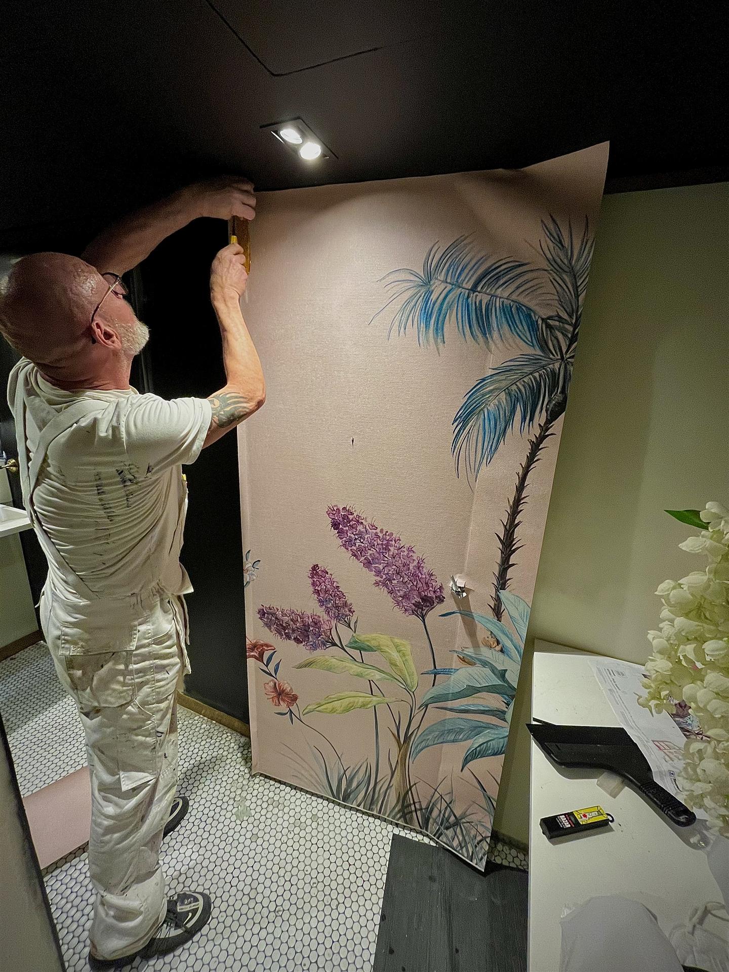 Decorator hanging large tropical wallpaper mural in restaurant, London